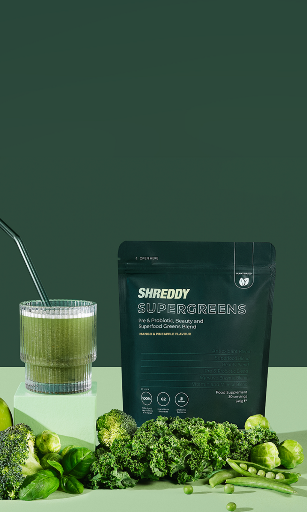 Shreddy SuperGreens package with a glass of green juice and fresh vegetables on a green background